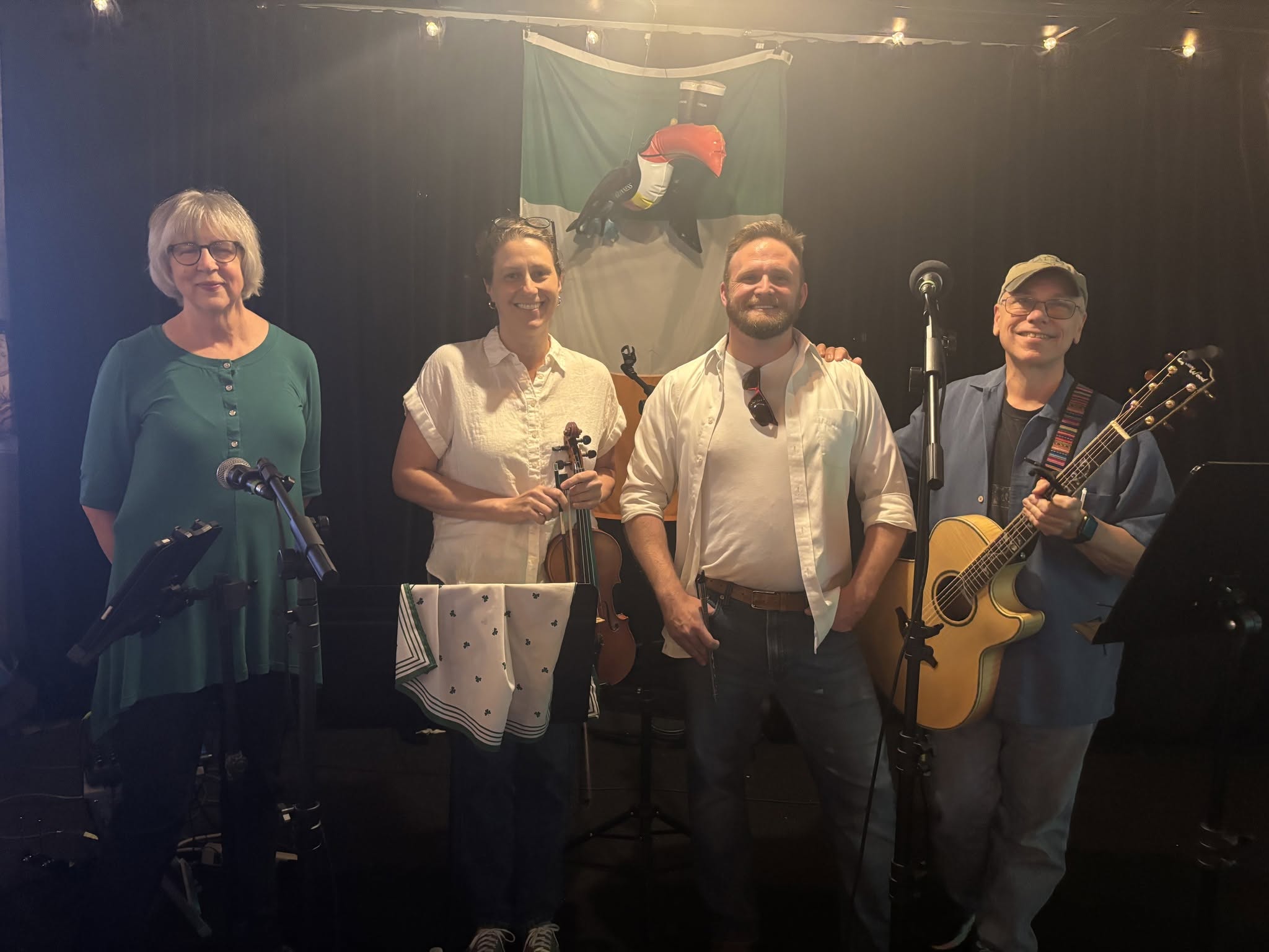 Four Far From Hibernia band members posing together with a fiddle and acoustic guitar.